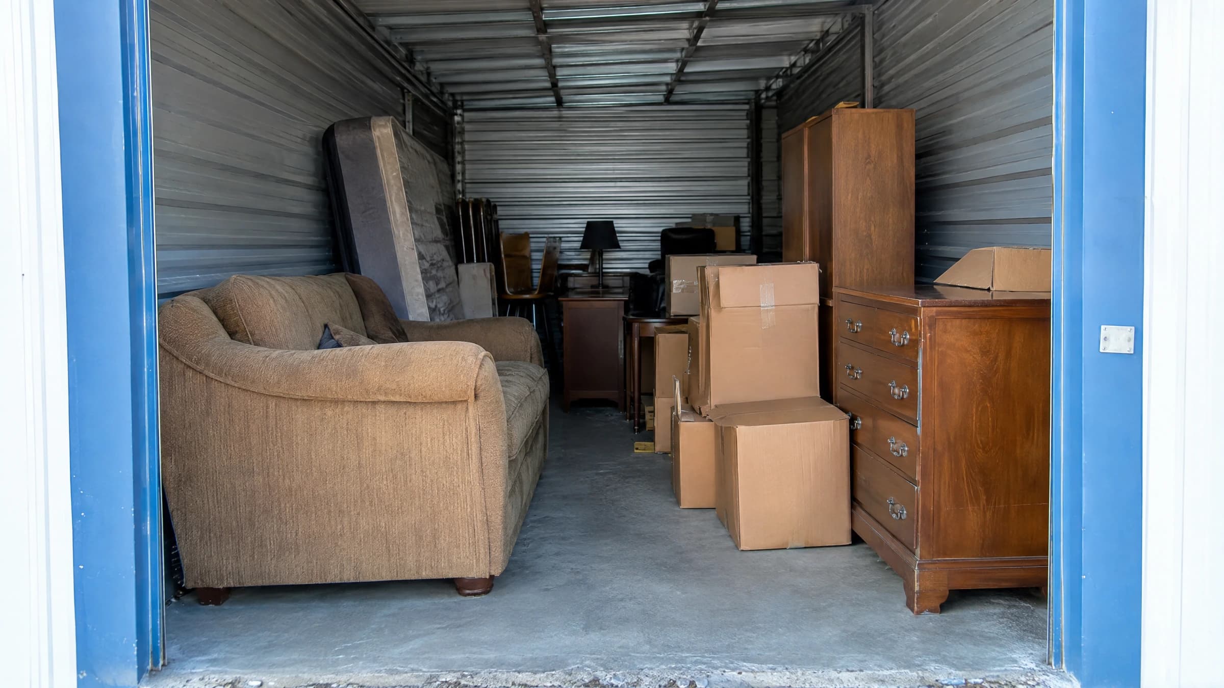 Unwanted furniture and closed boxes inside an open rented storage unit.