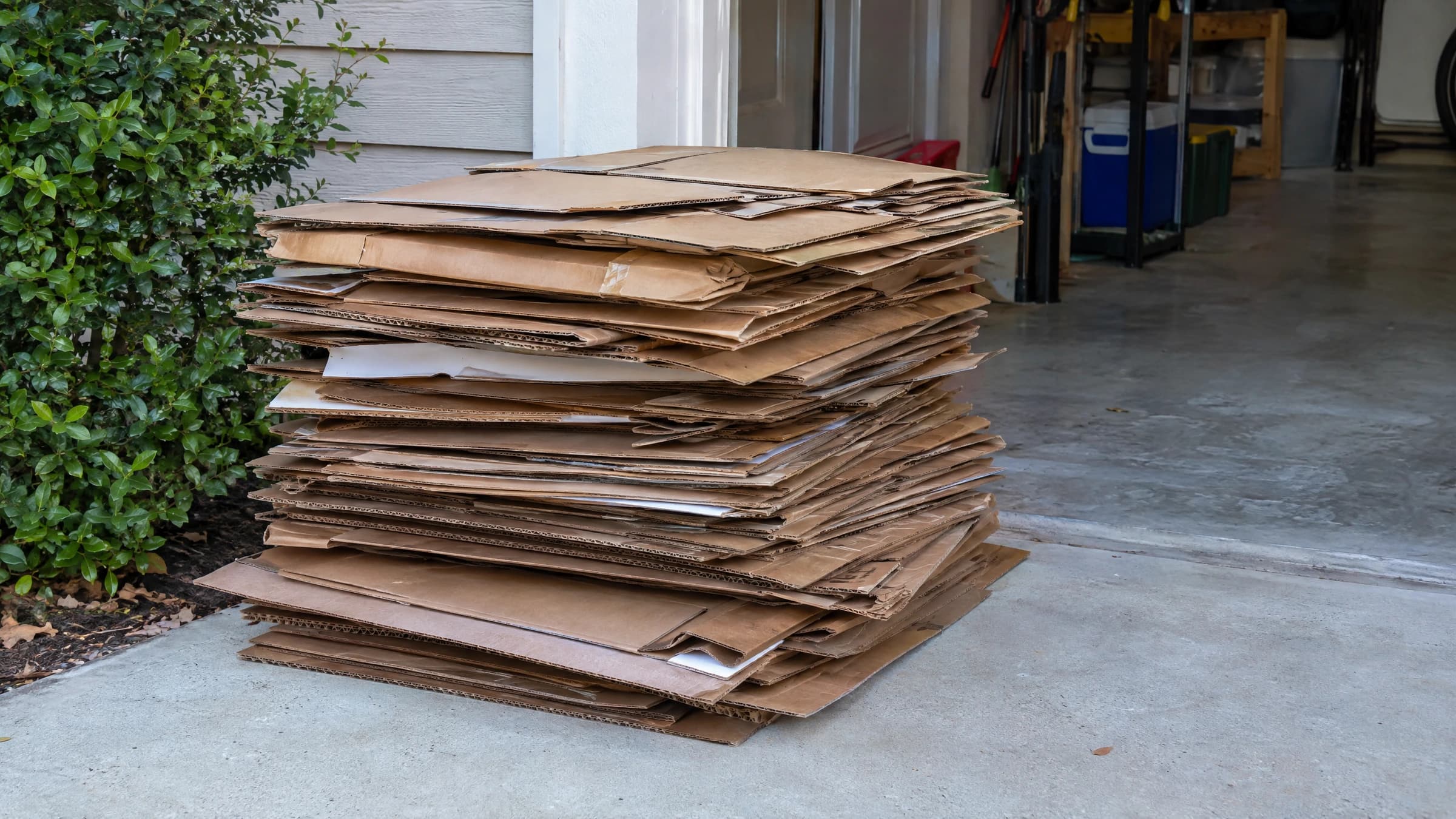 Flattened cardboard boxes stacked beside an open residential garage.