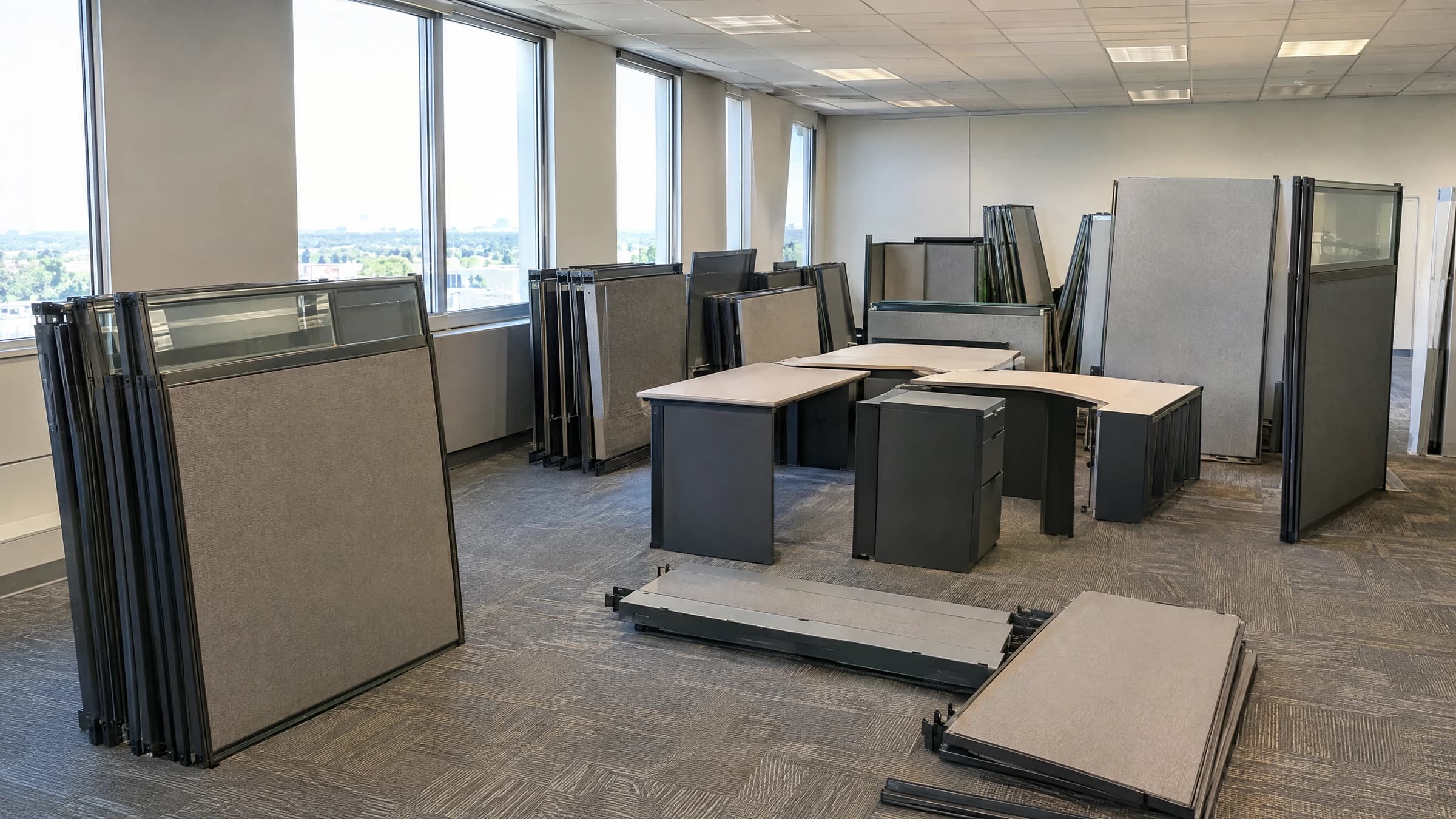 Detached cubicle panels and desk sections grouped on the floor of a vacant office.